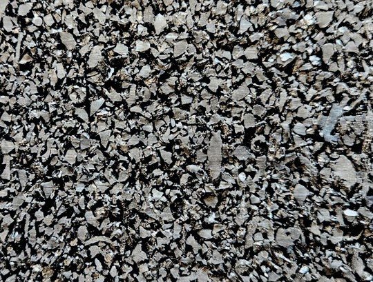 Gomma riciclata a granulo grosso, prevalentemente nera, con scaglie irregolari
