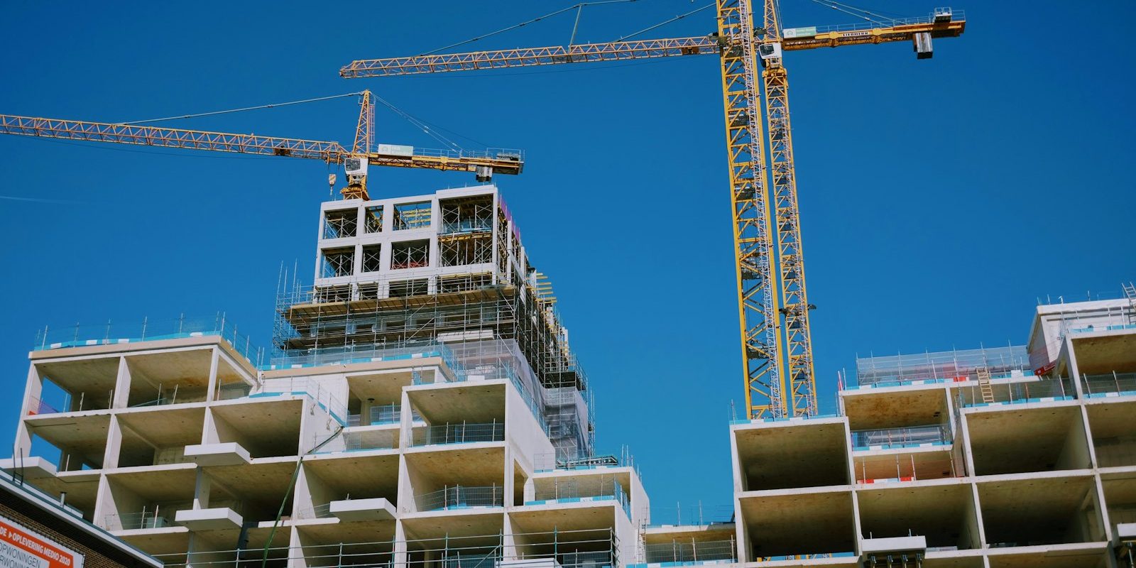 Edificio residenziale a più piani in costruzione, con pareti e solai a vista e due gru a torre