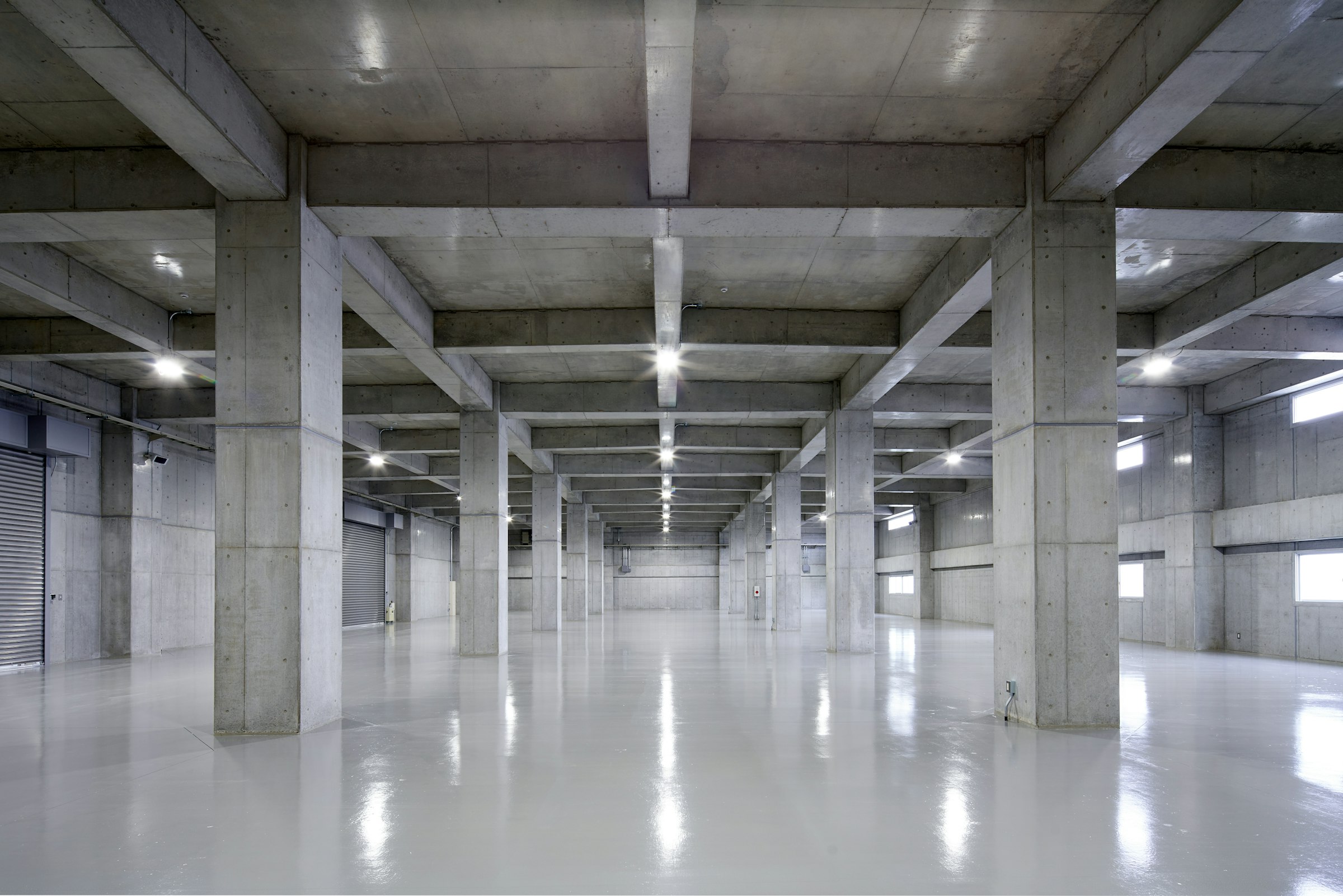 Grande sala in calcestruzzo a vista con pilastri, travi e pavimento lucido
